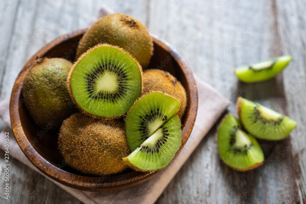 Fresh kiwi fruit in the bowl on wooden background